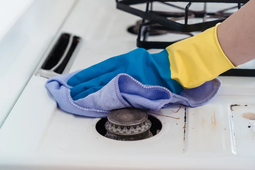 Gloved hand wiping a grimy gas hob with the grate lifted aside