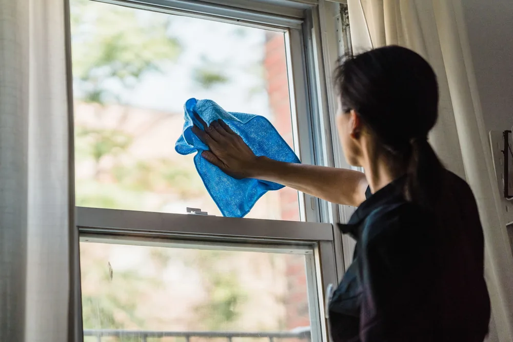 Woman wiping a sash window pane with a blue microfibre cloth