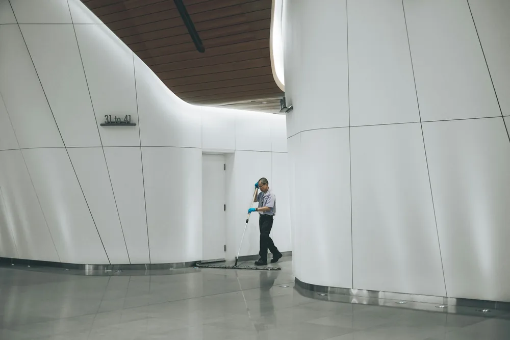 Cleaner pushing a flat dust mop along a white curved corridor