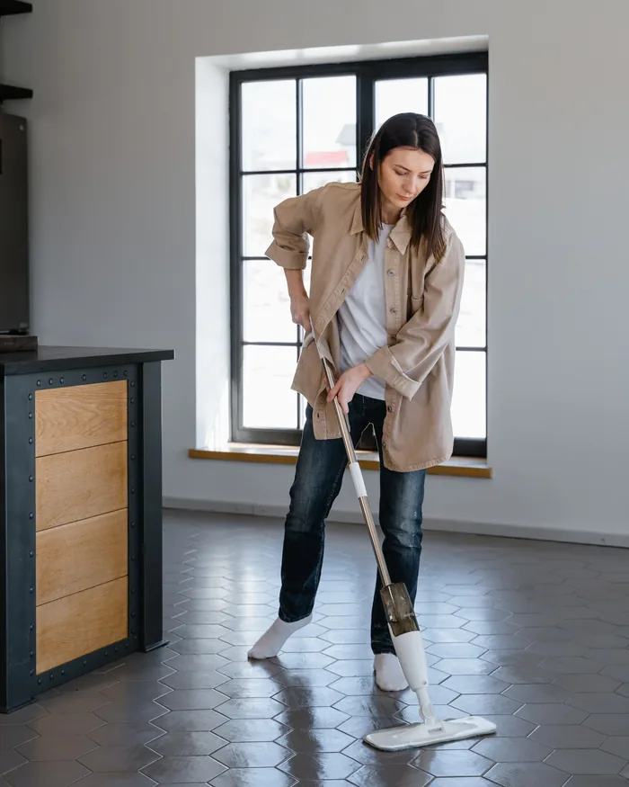 Woman mopping a grey hexagonal tiled floor beside a window